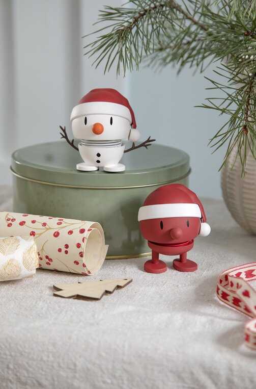 Figúrka veselých Hoptimistov Soft Santa Snehuliak a Soft Santa na zelenej plechovej darčekovej krabičke vedľa roliek ozdobného baliaceho papiera