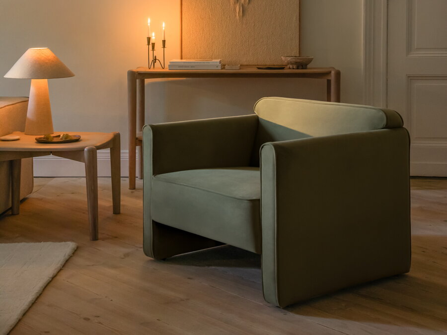 Zelené čalúnené kreslo v prítmí vedľa dreveného príručného stolíka so svietiacou stolovou lampou.