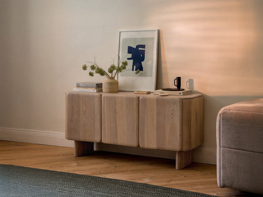 Minimalistická komoda Aggie z dubového dreva prírodnej farby, na ktorej sú položené rôzne dekorácie.