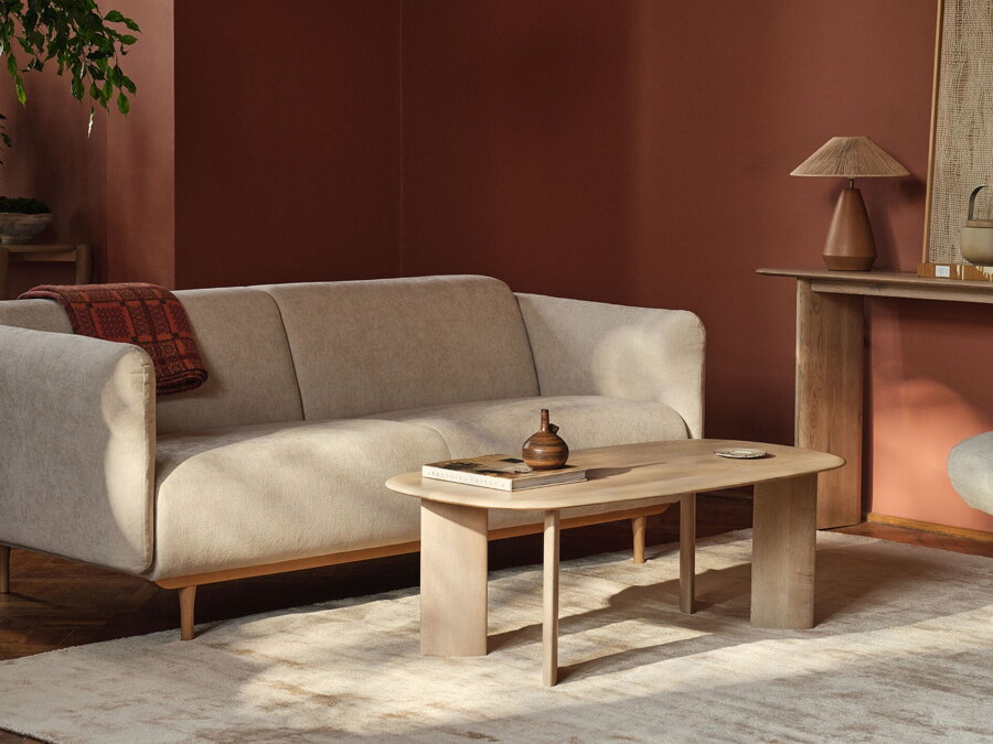 Obdĺžnikový konferenčný stolík Aggie z dubového dreva prírodnej farby v obývačke s béžovou sedačkou a hnedým konzolovým stolíkom so stolovou lampou.