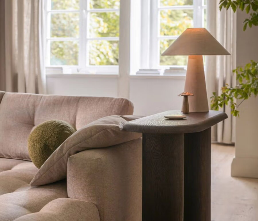 Tmavohnedý konzolový stolík so stolovou lampou v obývačke vedľa pohovky.