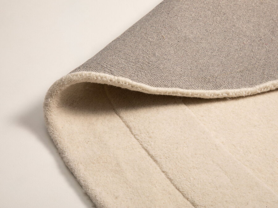 Záber na zahnutý okraj bieleho vlneného koberca.