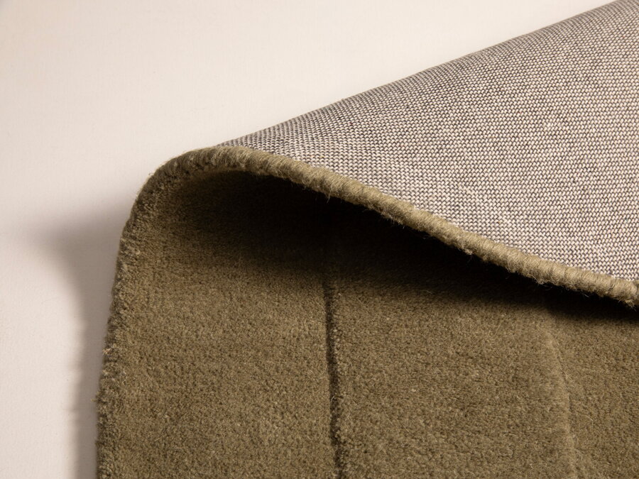 Záber na prehnutý okraj hnedozeleného koberca Cloria.