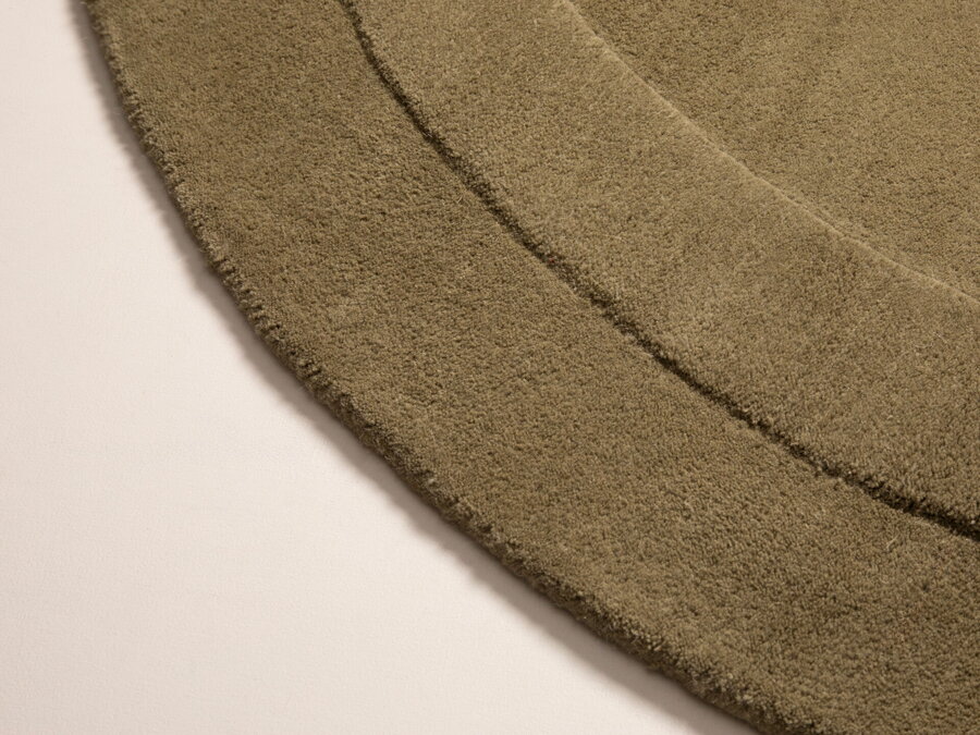 Detail na okraj a lem hnedozeleného koberca z polypropylénu v organickom tvare.
