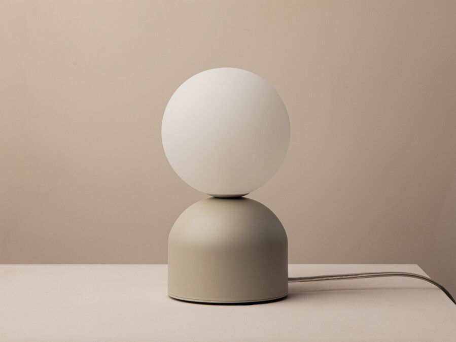 Stolová lampa Ely s matnou béžovou kovovou základňou a matným bielym skleneným tienidlom v tvare gule.