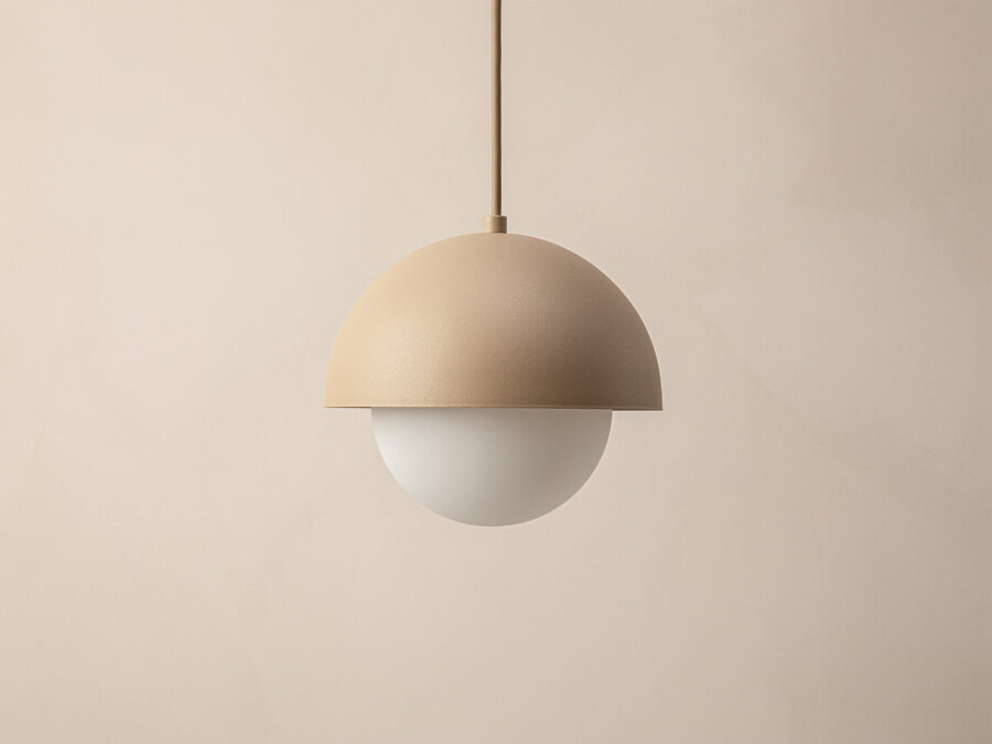 Závesná lampa Kora s tienidlom zo sklenenej gule matnej bielej farby zasadenej do polkruhového oceľového rámu pieskovej farby.