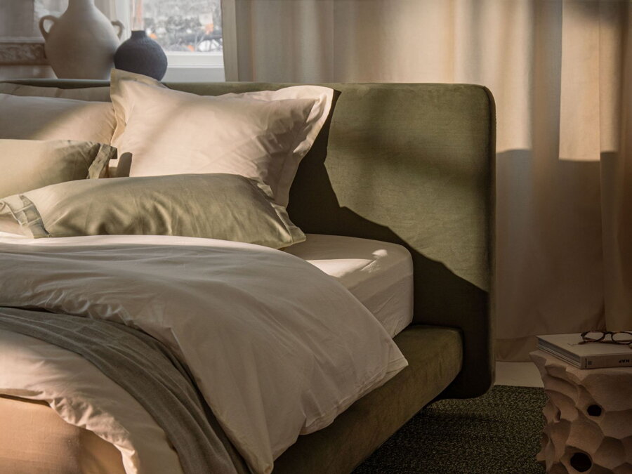 Detail na čelo manželskej postele Linea v čalúnení zelenej farby v spálni, do ktorej prenikajú podvečerné slnečné lúče.