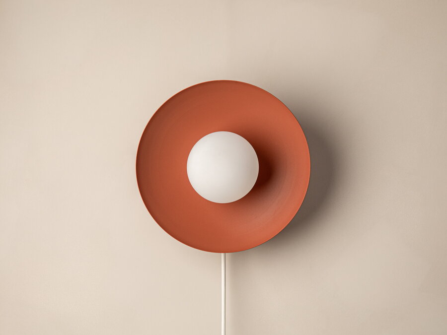 Nástenná lampa Mist, ktorá spája okrúhly kovový rám tehlovej farby s matnou bielou sklenenou guľou.
