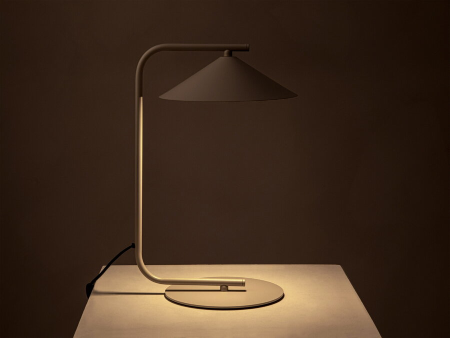 V tme rozsvietená stolová lampa Nocte s tienidlom v tvare kužela, z kvalitného matne lakovaného kovu béžovej farby.