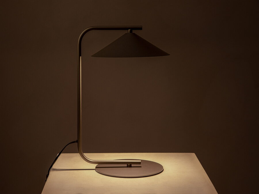 V tme rozsvietená stolová lampa Nocte s tienidlom v tvare kužela, z kvalitného matne lakovaného kovu hnedej farby.