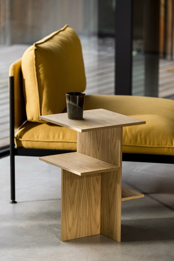 Elegantný nočný stolík Atik z matnej dubovej dyhy prírodnej farby vedľa žltého kresla.