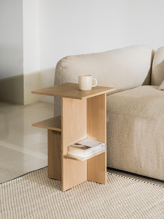 Minimalistický nočný stolík Atik z matnej dubovej dyhy prírodnej farby vedľa béžovej pohovky.