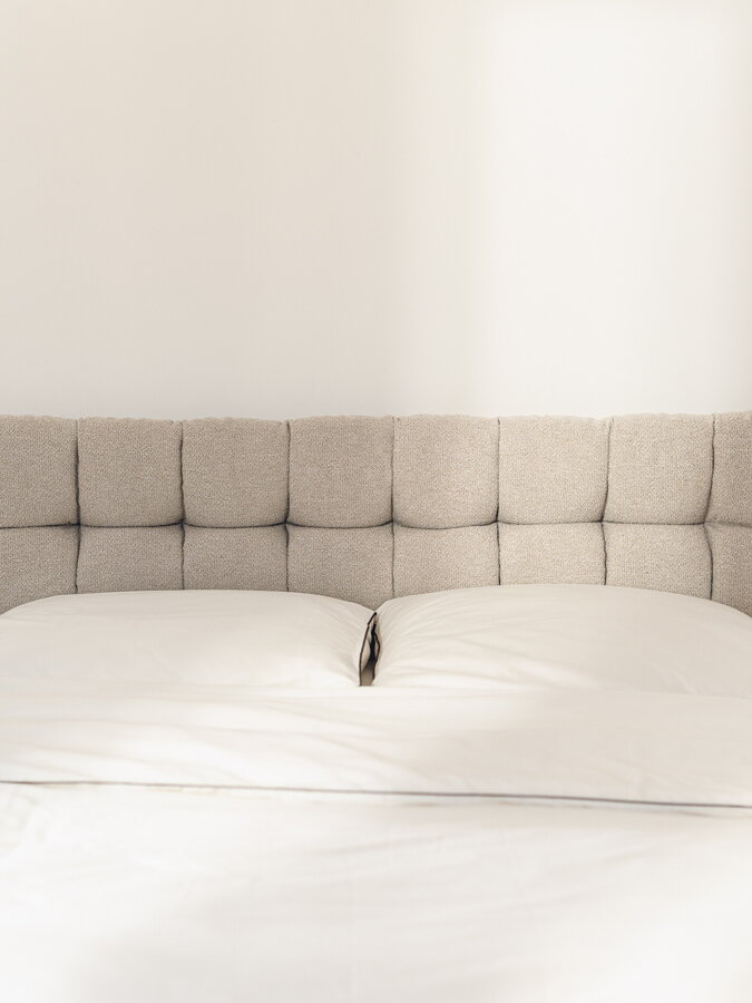 Béžové čelo postele Bolbi v čalúnení Boucle, zavesené na bielej stene nad posteľou.