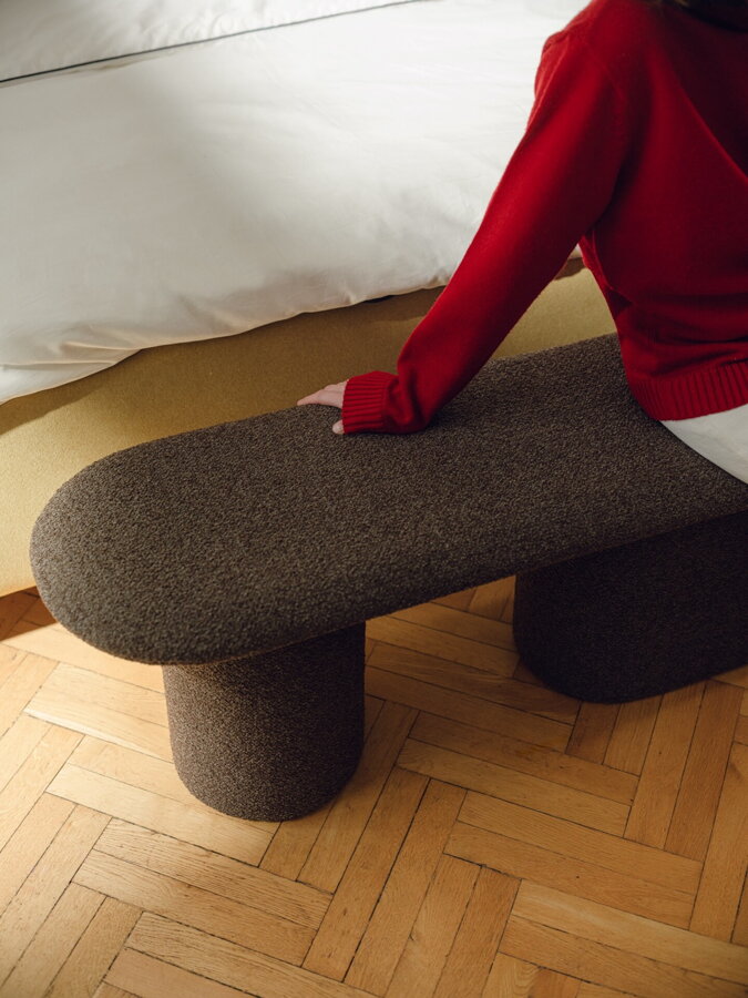 Osoba v červenom pulóvri sediaca na hnedej čalúnenej lavici.