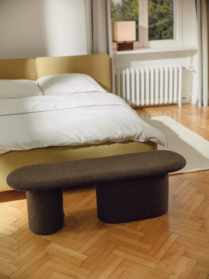 Čokoládovo hnedá čalúnená lavica v spálni pred manželskou posteľou na drevenej podlahe.