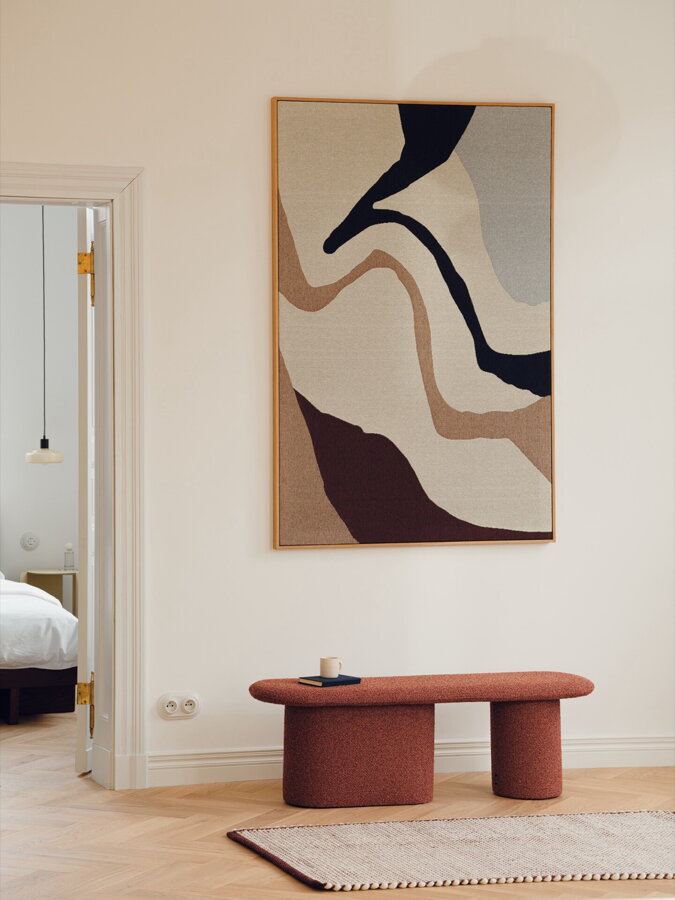 Čalúnená lavica Rull tehlovej farby v chodbe pri stene, na ktorej visí abstraktný obraz.