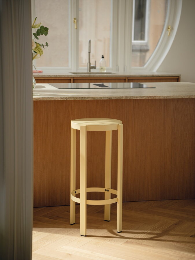 Muž sediaci na svetložltej barovej stoličky pri kuchynskom ostrovčeku.