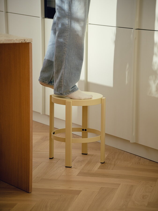 Osoba stojaca na svetložltom stolíku/stoličke v kuchyni.