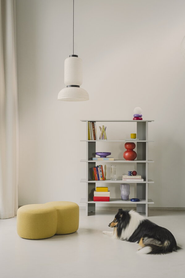 Červená polica, na ktorej sú položené rôzne predmety, v miestnosti so žltým pufom a čiernym psom.