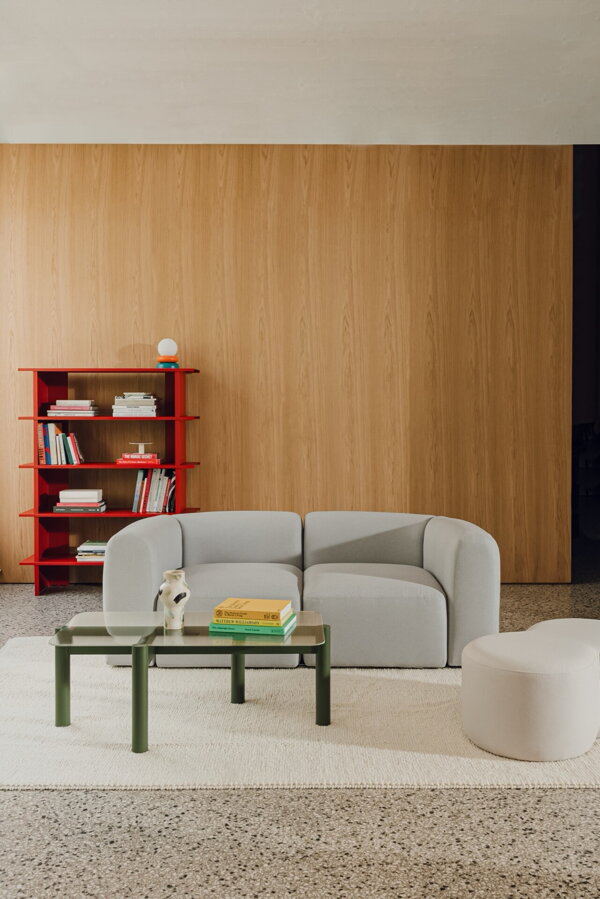 Červená polica, na ktorej sú položené rôzne predmety, v miestnosti so sivou pohovkkou a zeleným konferenčným stolíkom.