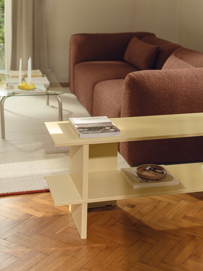 Svetložltá nízka kovová polica v obývačke s béžovým kobercom a tehlovou pohovkou.