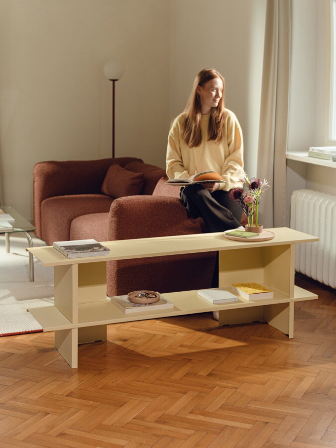 Svetložltá nízka kovová polica v obývačke so ženou sediacou na opierke hnedej pohovky.