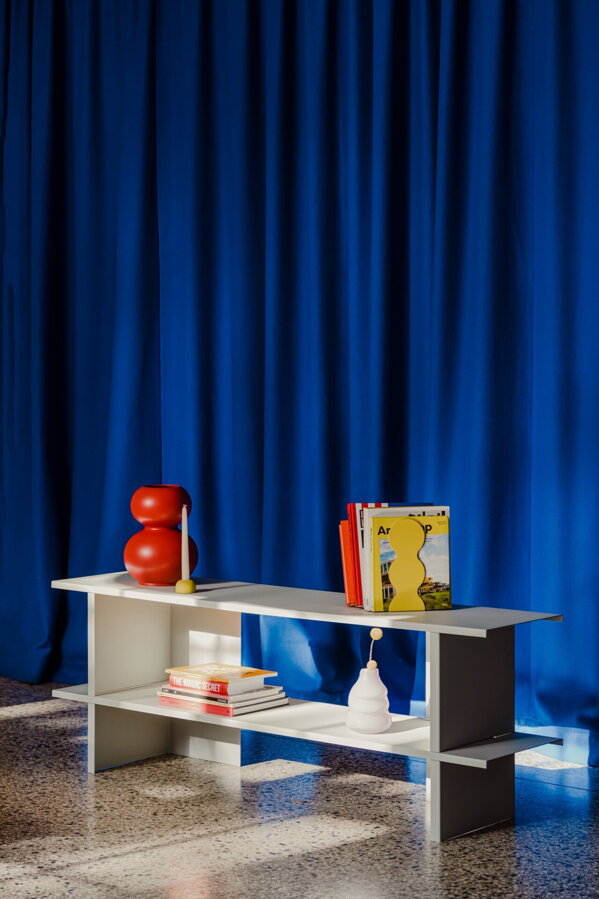 Sivá nízka kovová polica v miestnosti s tmavomodrou stenou.