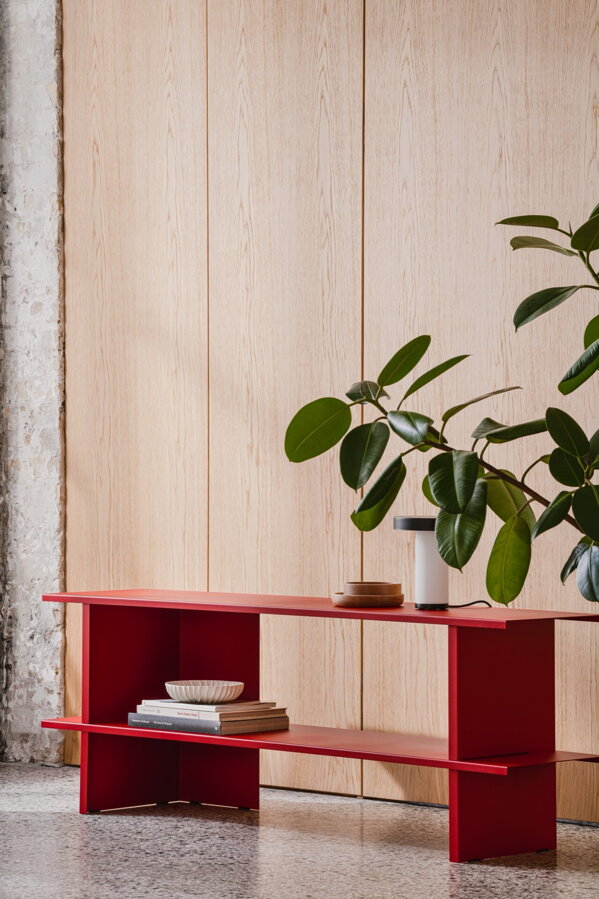 Červená kovová nízka polica v miestnosti pred izbovou rastlinou.