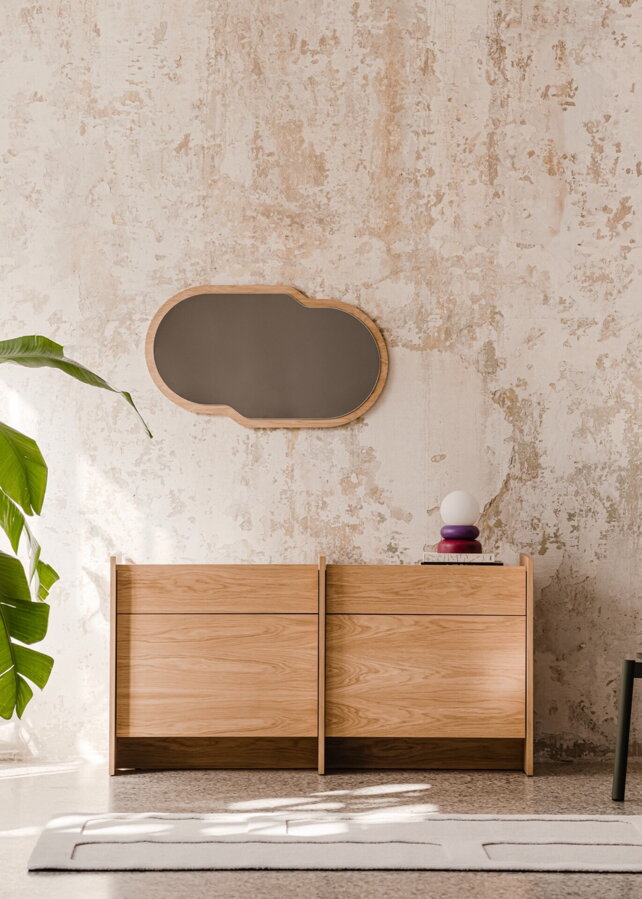 Dubová komoda s dvierkami pri betónovej stene v miestnosti s izbovou rastlinou.
