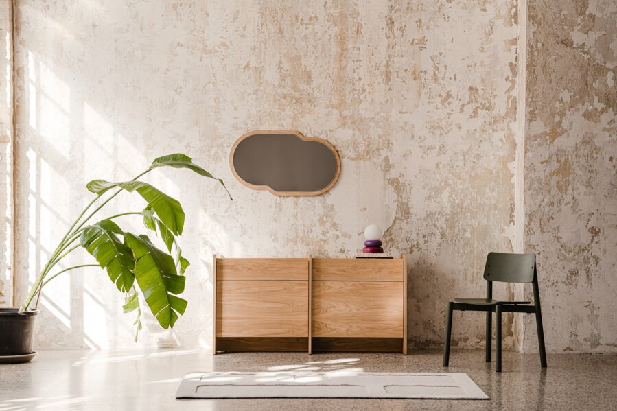 Dubová komoda s dvierkami pri betónovej stene v miestnosti s izbovou rastlinou a čiernou stoličkou.