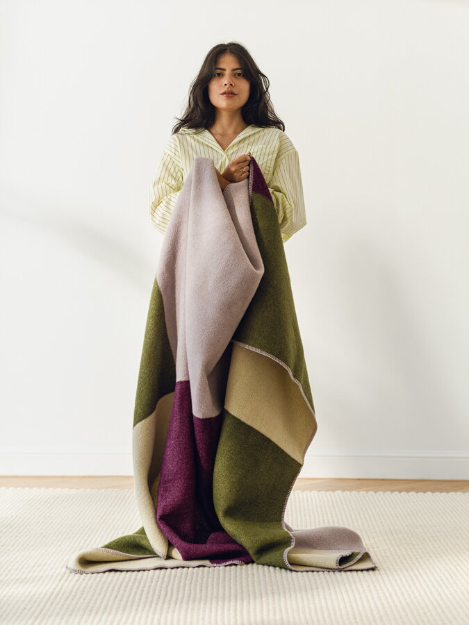 Stojaca žena zabalená do zeleno fialovej vlnenej deky.