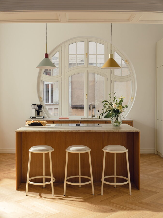 Tri béžové barové stoličky s čalúneným sedákom a kovovým rámom za kuchynským ostrovčekom.