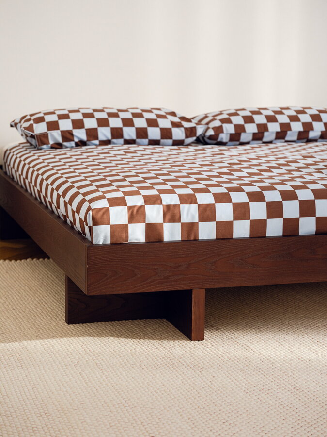 Tmavohnedá drevená posteľ v spálni s hnedou kockovanou perinou.