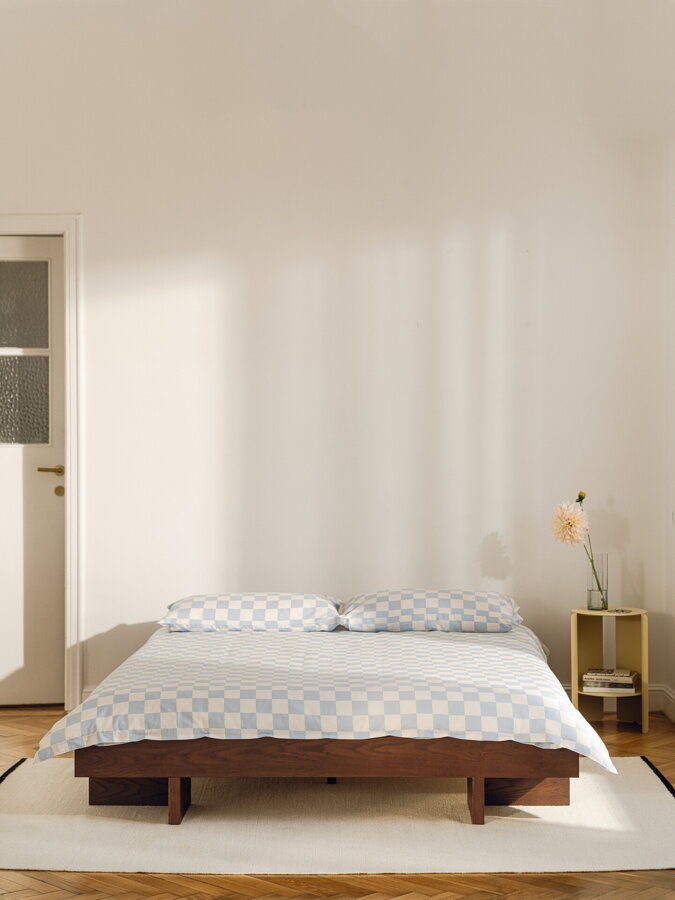 Tmavohnedá jaseňová manželská posteľ vo svetlej spálni na bielom koberci.