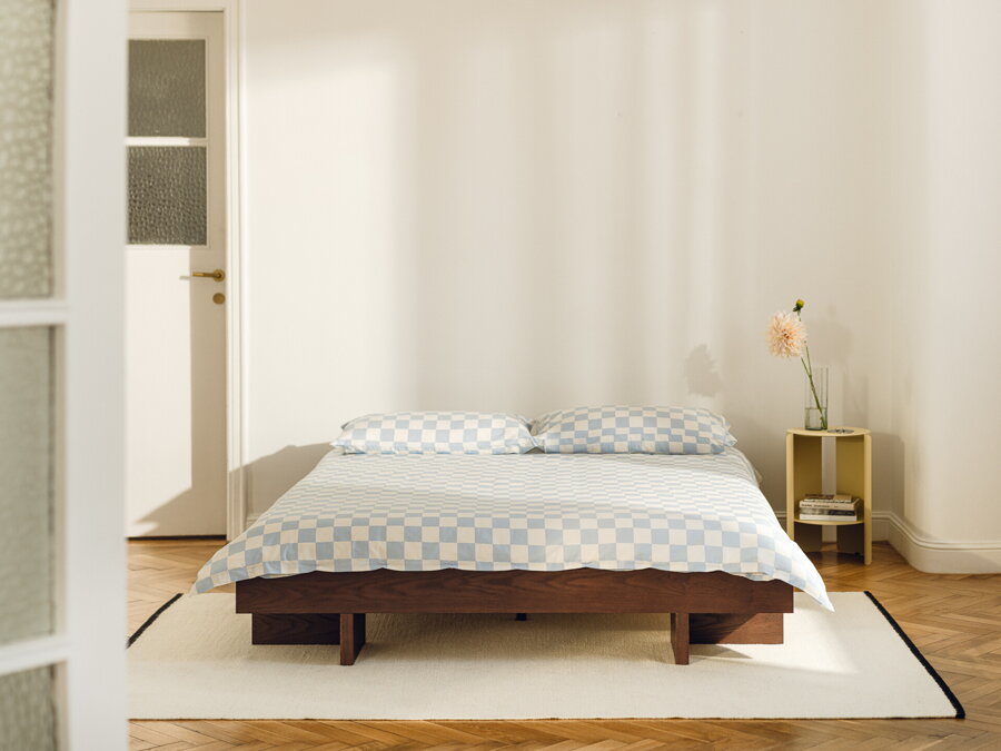 Tmavohnedá jaseňová manželská posteľ vo svetlej spálni na bielom koberci.