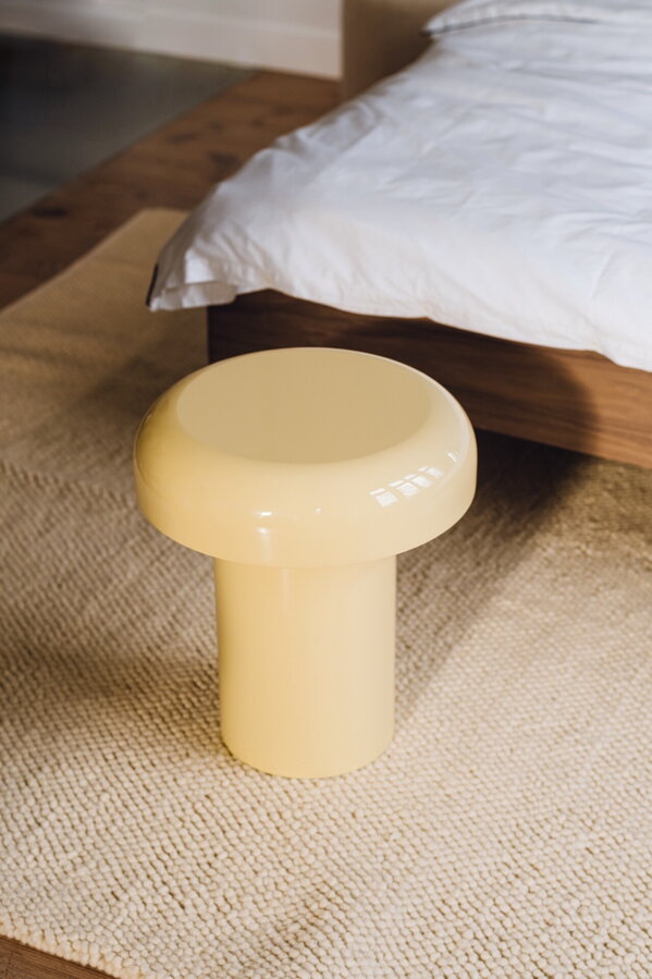 Svetložltý príručný stolík vedľa postele na podlahe.