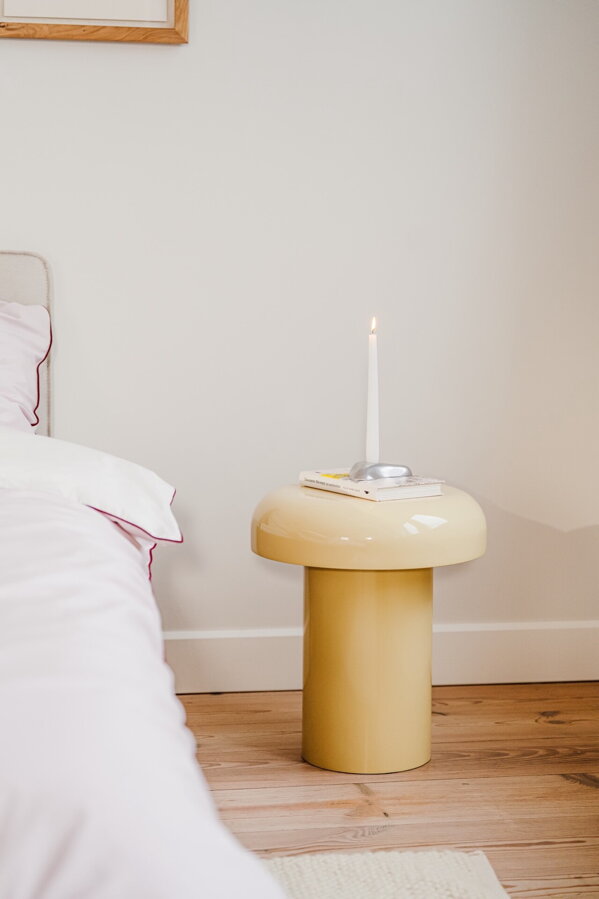 Svetložltý príručný stolík vedľa postele na podlahe.