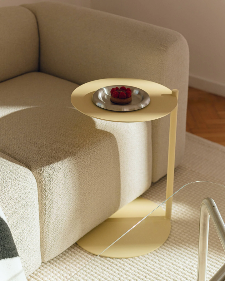 Oceľový príručný stolík Ande svetložltej farby s miskou s malinami vedľa béžovej pohovky.
