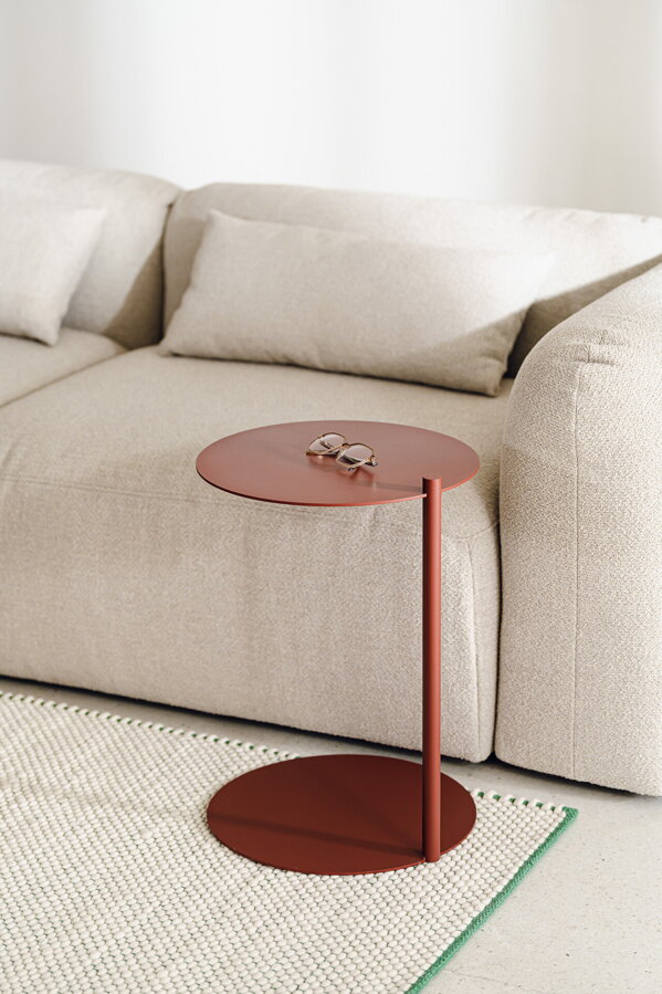 Oceľový príručný stolík Ande červenej farby vedľa béžovej pohovky.