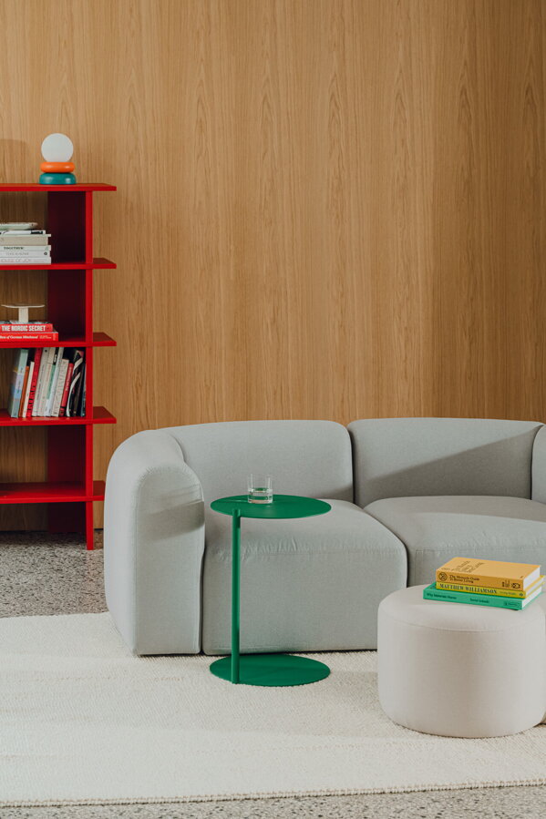 Oceľový príručný stolík Ande zelenej farby vedľa svetlosivej pohovky a sivého pufu na béžovom koberci.