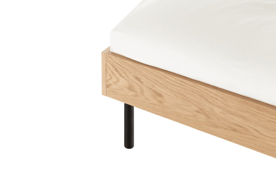 Detail na dubový rám a oblé čierne nohy postele.