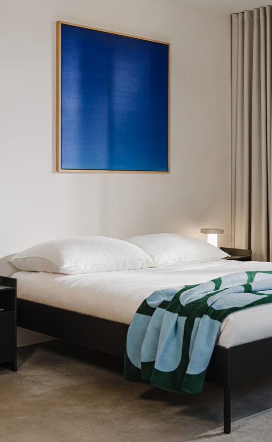 Čierna melamínová manželská posteľ v spálni na drevenej podlahe, nad posteľou visí veľký modrý abstraktný obraz.