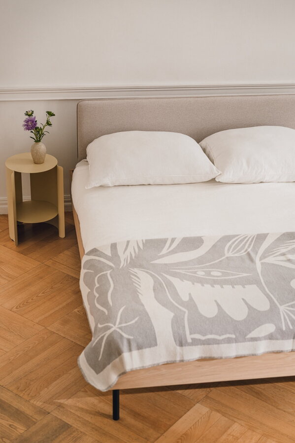 Dubová manželská posteľ s pieskovým čalúneným čelom v spálni na drevenej podlahe vedľa dubového príručného stolíka.