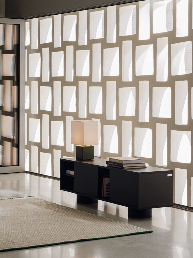 Čierny nízky TV stolík na sivej podlahe pred béžovým kobercom.