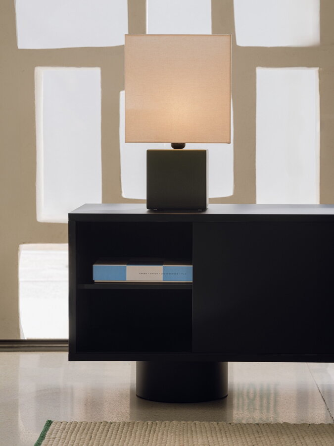 Stolová nočná lampa položená  na čiernom tv stolíku s pootvorenými dvierkami.