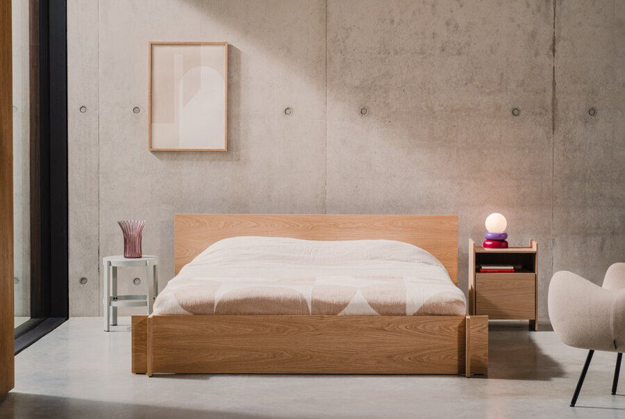 Masívna dubová manželská posteľ v spálni s veľkou presklenou stenou a stenou z betónového panelu.