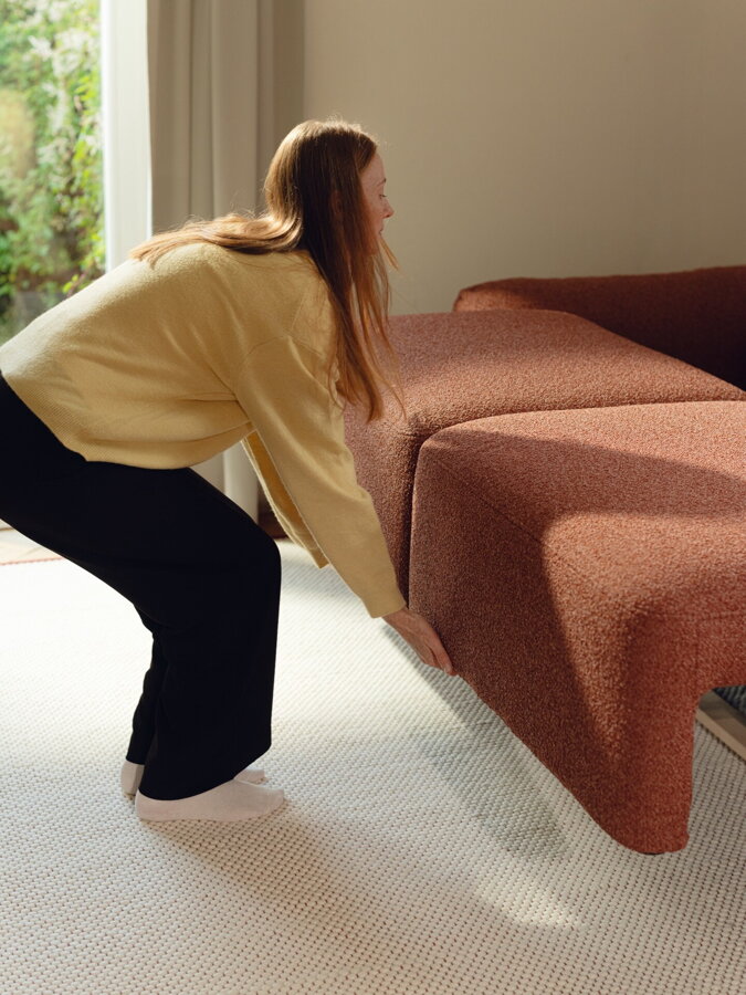 Žena rozkladajúca rozkladaciu pohovku v tehlovej farbe.