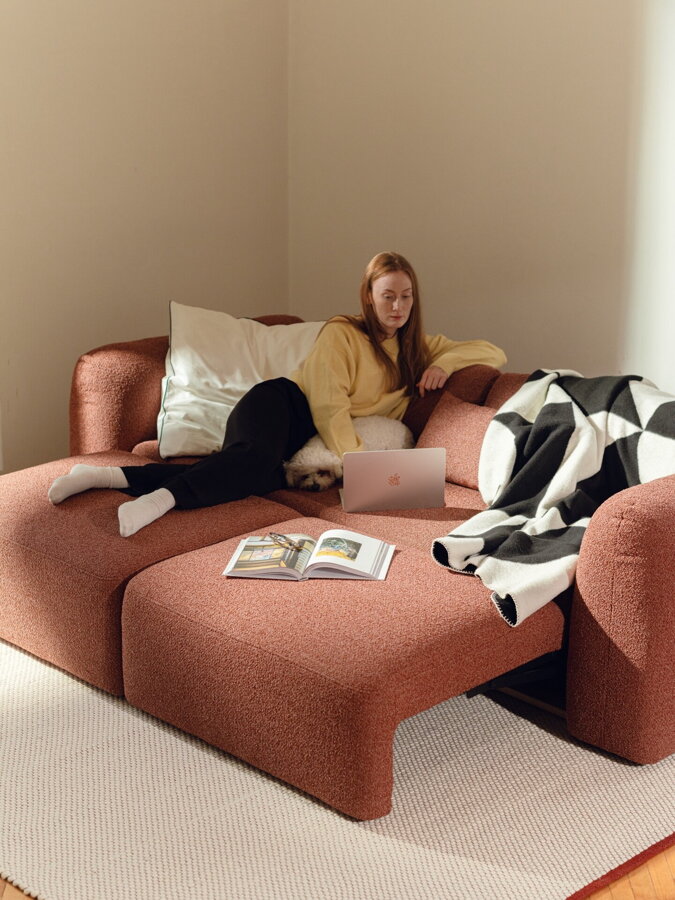 Tehlová oranžová 3-miestna pohovka v rozloženom stave, na ktorej leží žena.