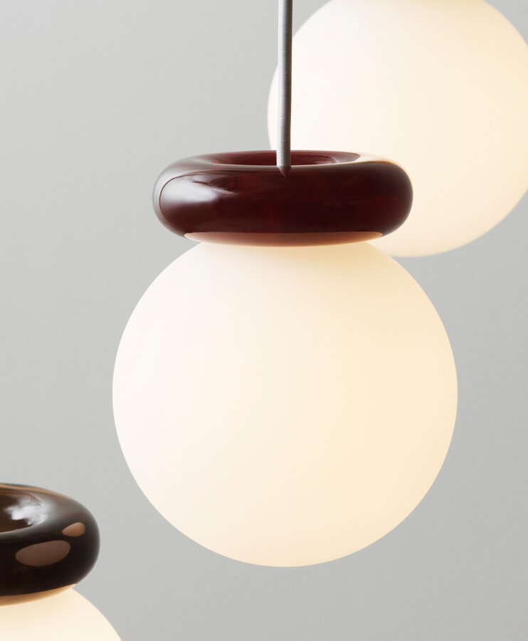 Závesná lampa Hinx kombinujúca guľu z matného bieleho skla a efektný sklenený prstenec v tmavočervenej farbe.