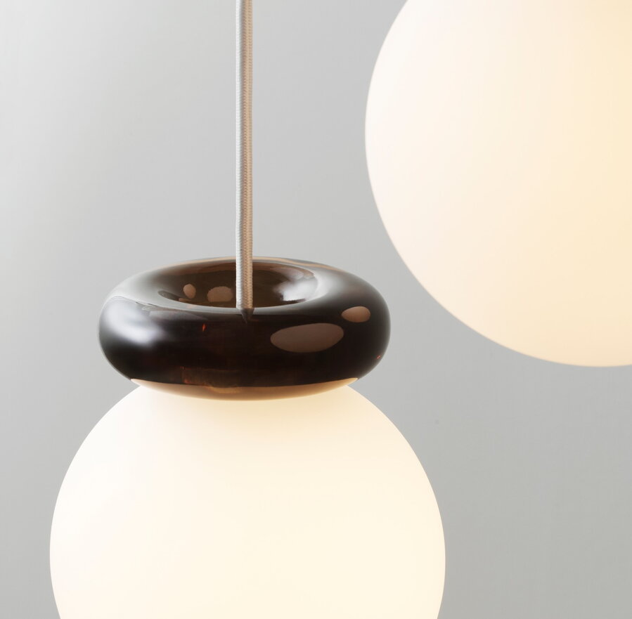 Závesná lampa Hinx kombinujúca guľu z matného bieleho skla a efektný sklenený prstenec v tmavohnedej farbe.